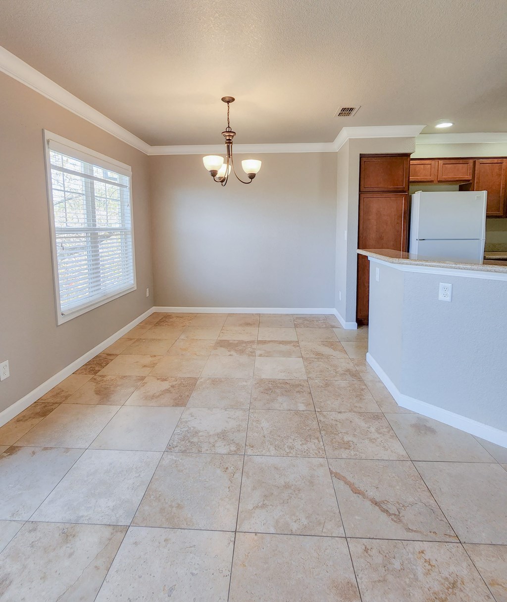 View of dining room with chandelier, peak into kitchen with brown cabinets, and white appliances