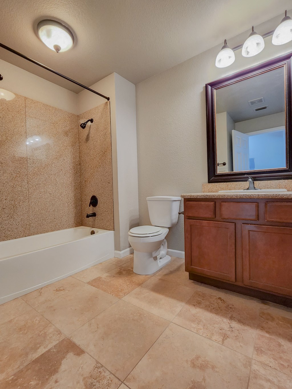 View of large bathroom, with tiled tub shower combo, toilet, vanity and sink, large mirror, and lighting