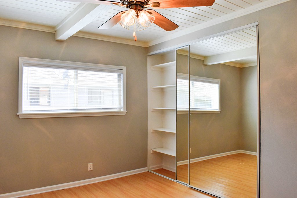 View of other side of bedroom with wood look flooring, floor to ceiling sliding glass mirror closet with built in shelving, and ceiling fan