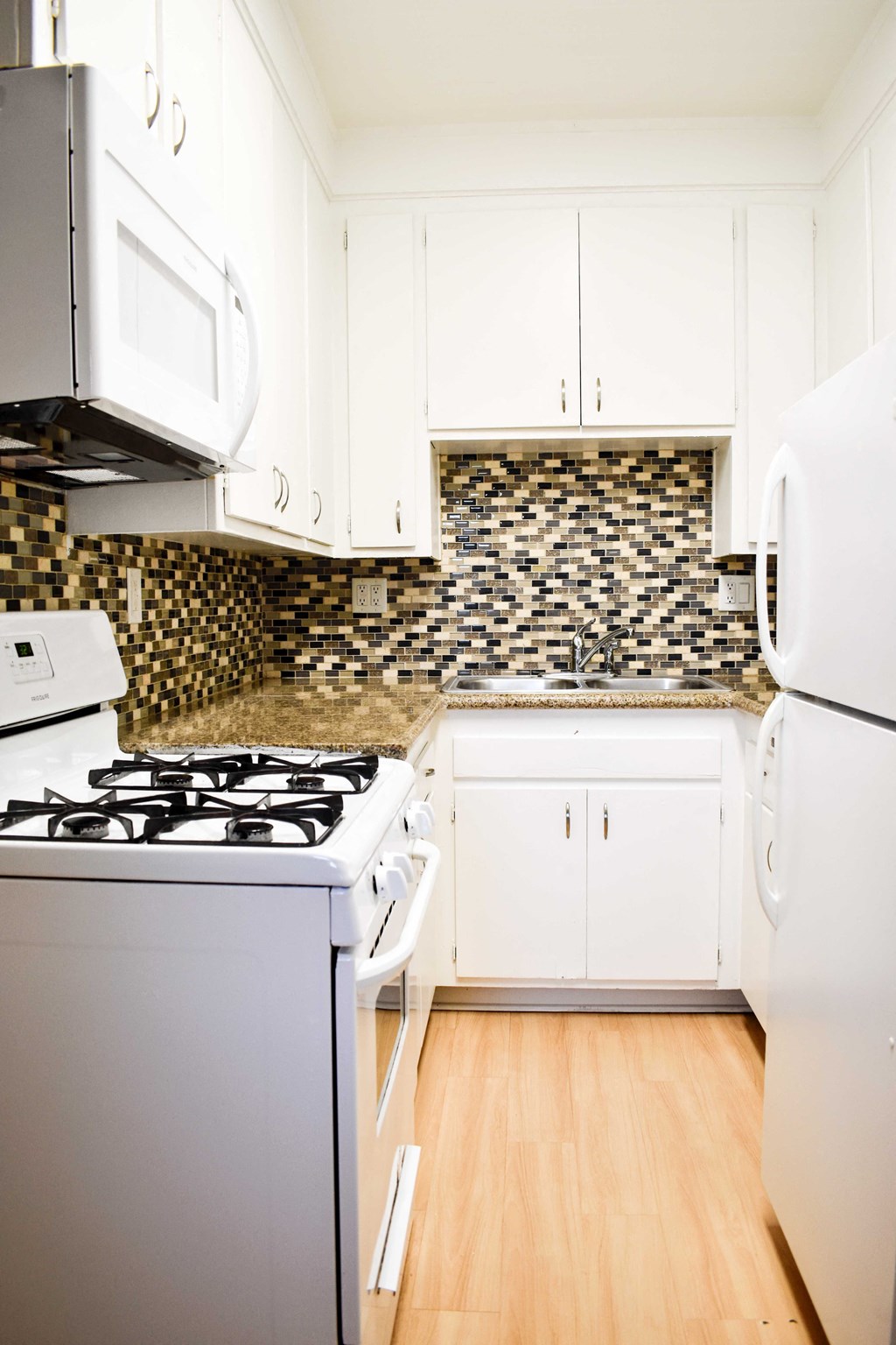View of kitchen with white cabinets, white appliances and wood look flooring