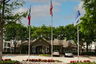 View of exterior leasing office with flags flying high, and lush trees