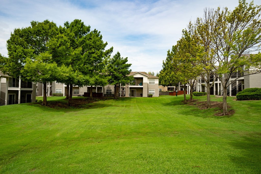 Large open lush grassy area in between building with green blooming trees