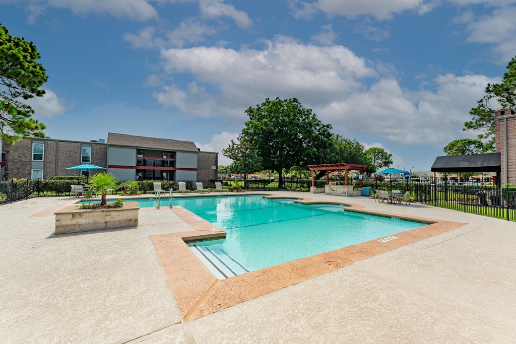 Gated community pool with lounge chairs, seating under umbrellas, and grilling station under pergola