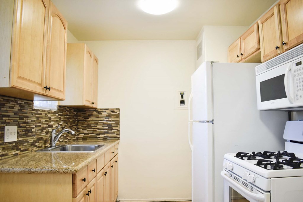 View of kitchen with stone counters, white appliances, and brown cabinets