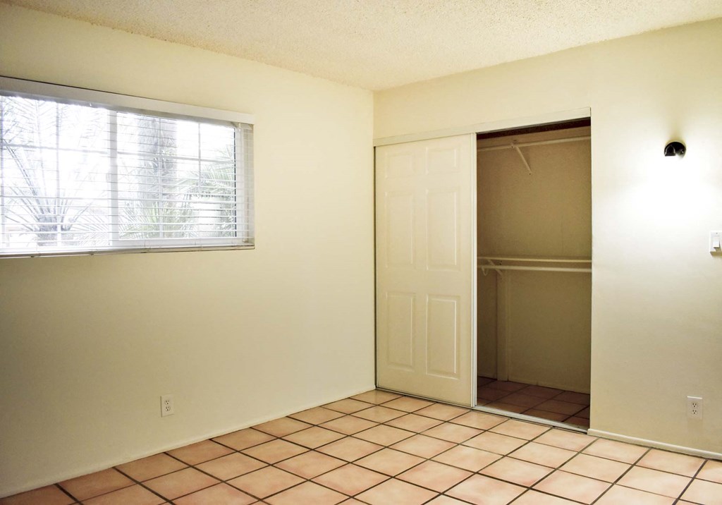 View of bedroom with tile flooring, well lit window, and sliding door closet