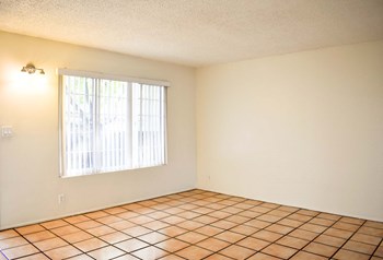 living area with large window, white walls, and brown tiles