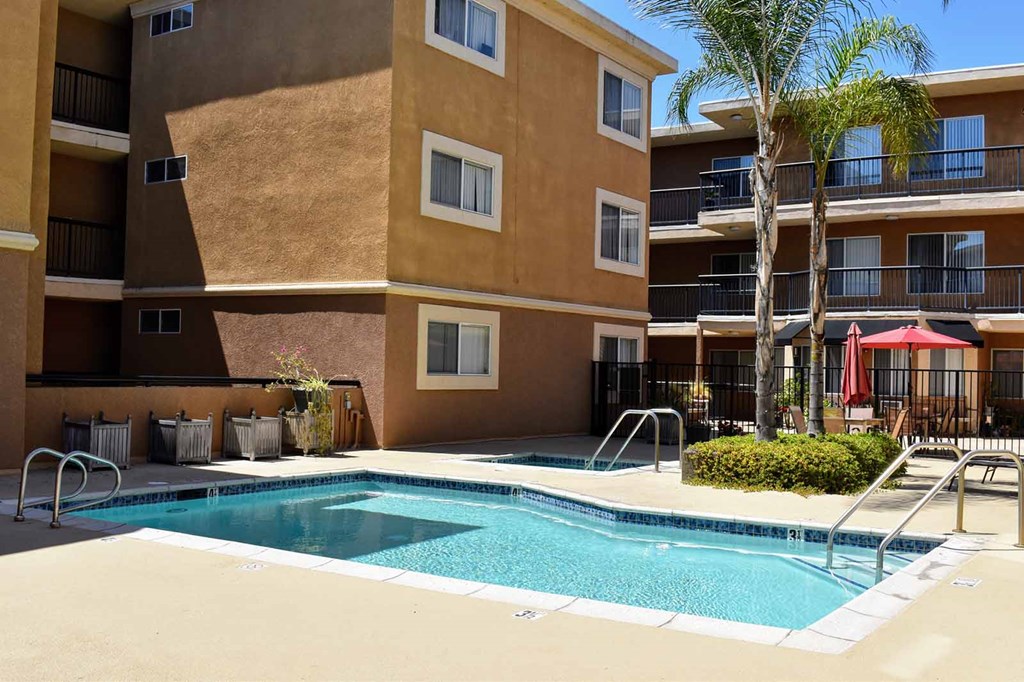 View of fated community pool with spa, exterior buildings and tropical landscaping in the background