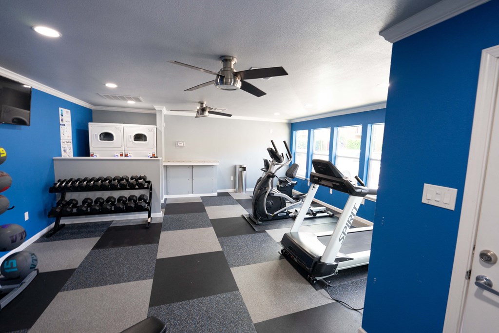 View of community gym featuring treadmill, eliptical, stationary bike, free weights, and partial view of laundry facility