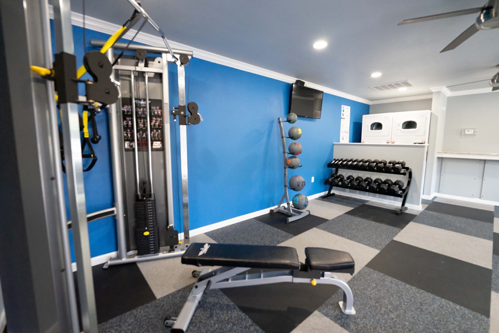 View of community gym featuring treadmill, eliptical, stationary bike, free weights, and partial view of laundry facility