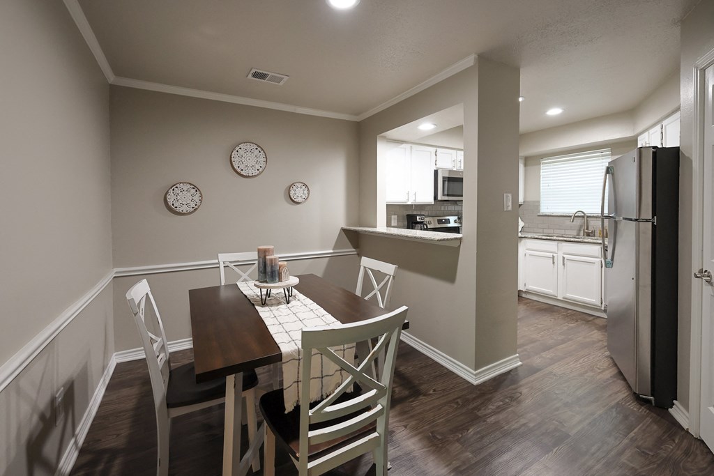 a dining room with a table and chairs and a kitchen in the background