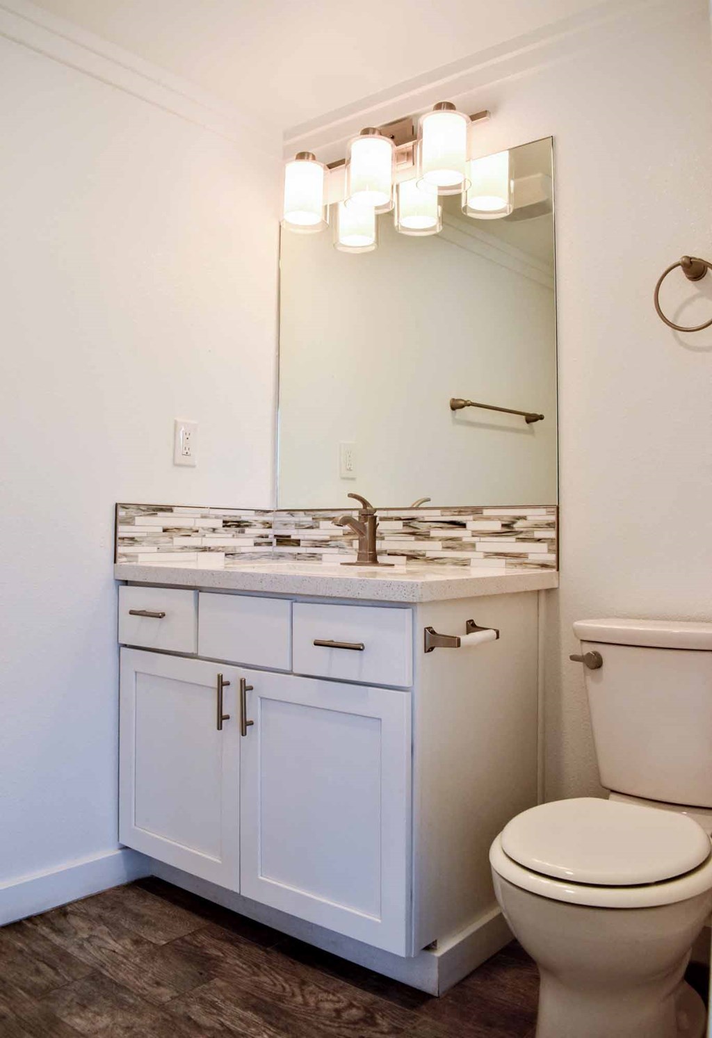 Bathroom with in laid sink, white cabinets, large well lit mirror, and toilet