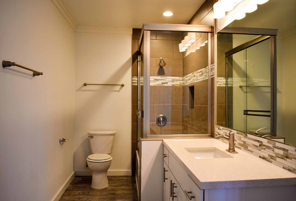 bathroom with in laid sink, white cabinets, large well lit mirror, toilet and tiled tub shower combo