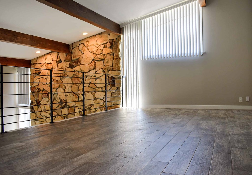 loft view looking towards stone fireplace with well lit windows and wood look flooring