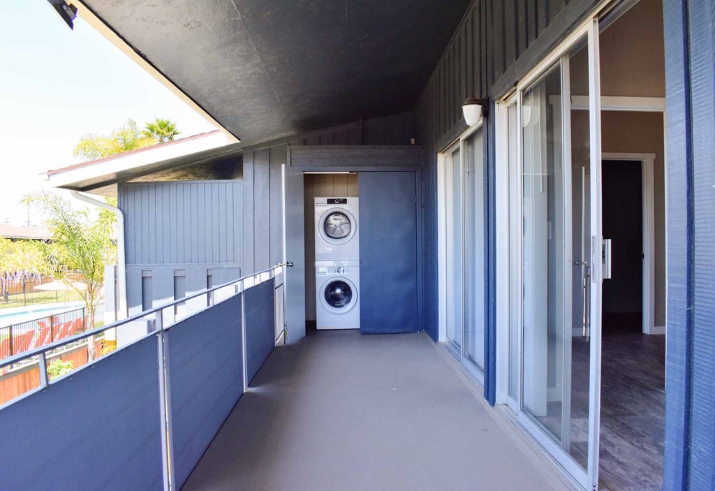 private balcony with sliding glass door open into home, and stacked washer and dryer in outside utility closet