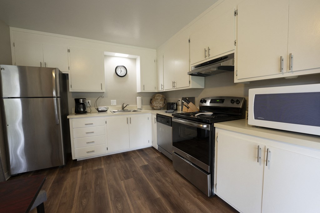 view of furnished model kitchen, with stainless appliances, wood look flooring, white cabinets, and well decorated