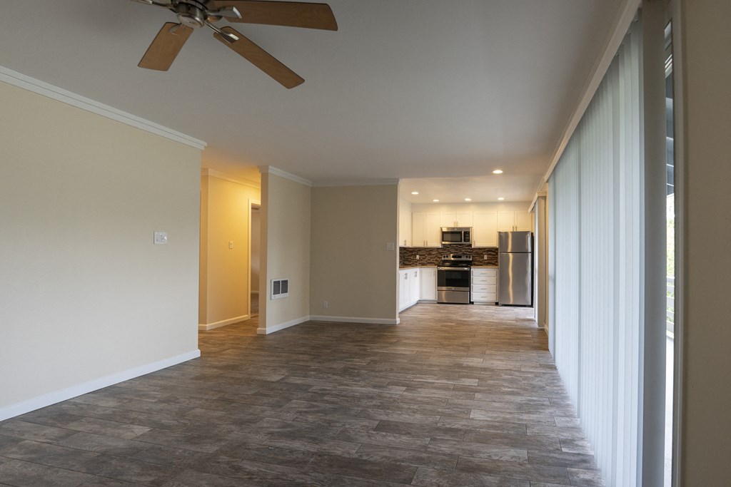 a living room with a ceiling fan and a kitchen in the background