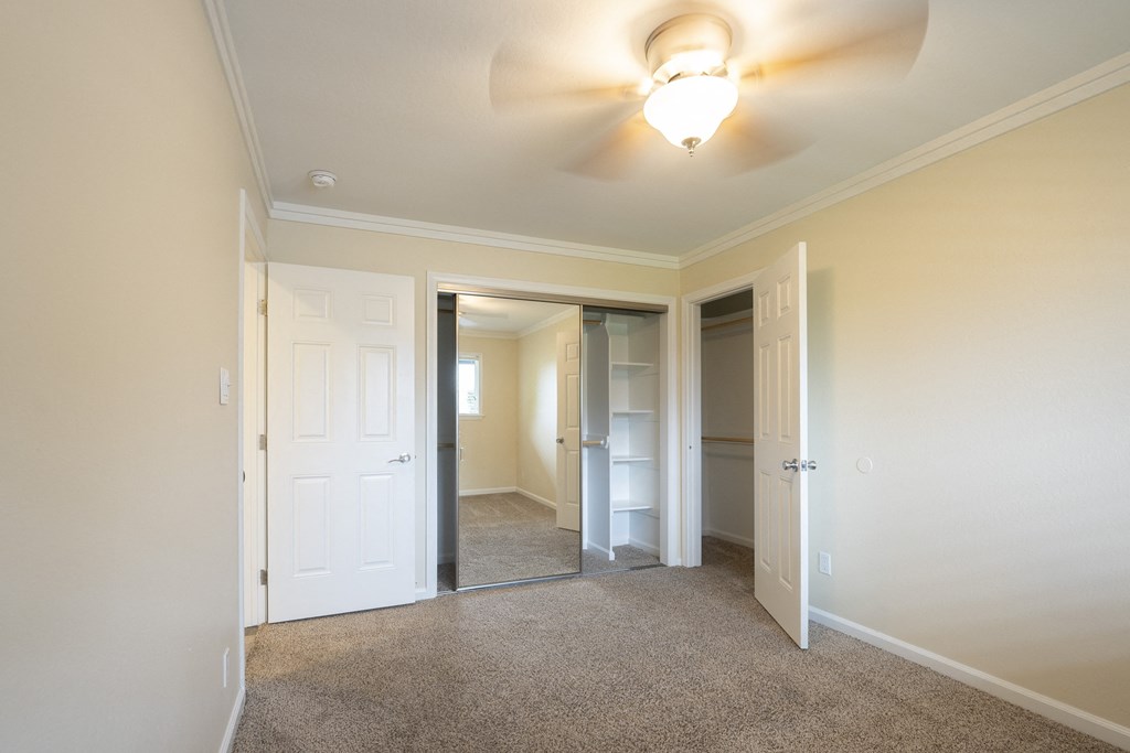 a bedroom with a ceiling fan and a closet with a mirrored door