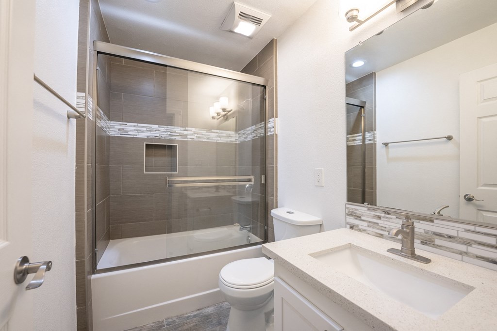 bathroom with in laid sink, large mirror with lighting, toilet, and tub shower combo