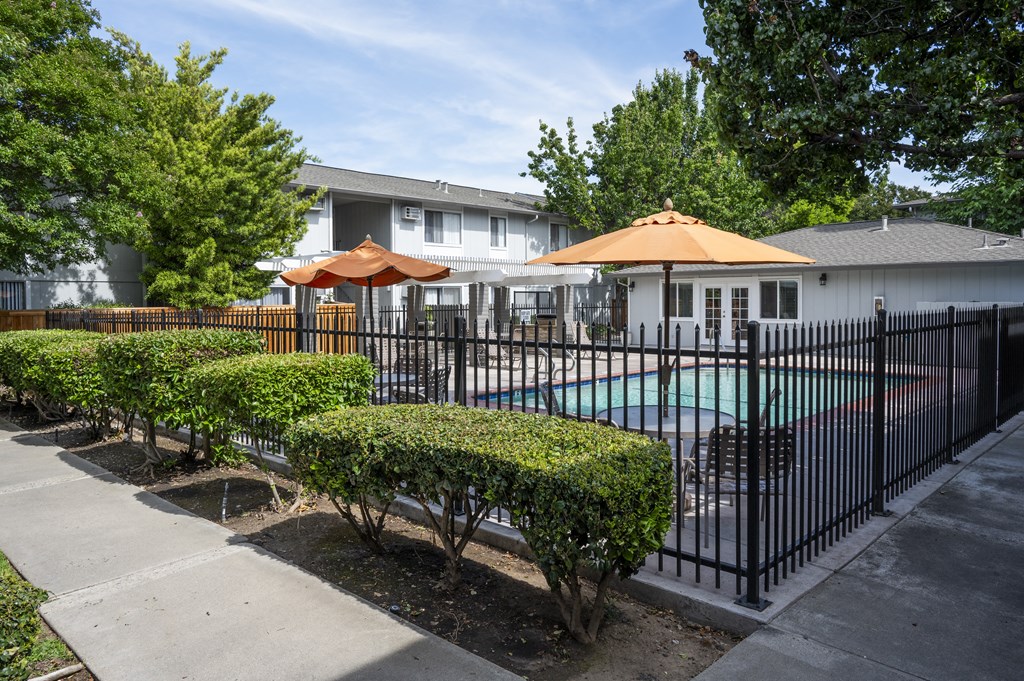 a yard with a pool and umbrellas in front of an apartment