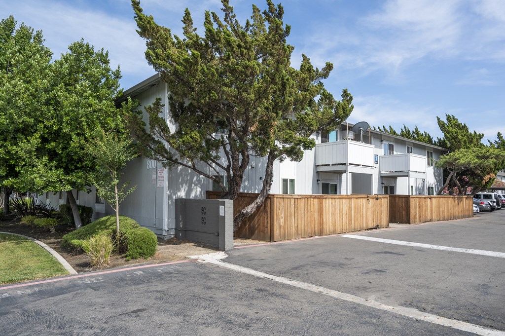 the exterior of an apartment with a wooden fence and a parking lot