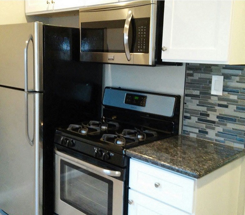 kitchen with stainless appliances, stone counters, tile backsplash, and white cabinets