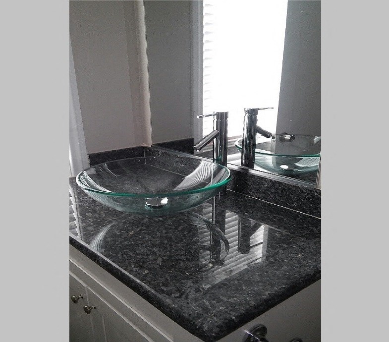 stone bathroom vanity top with glass vessel sink and large mirror.