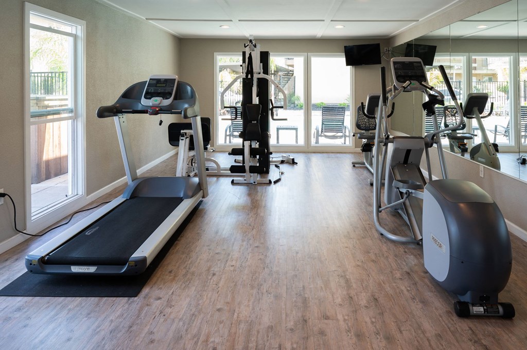 a gym with cardio equipment and windows in a building with wood floors