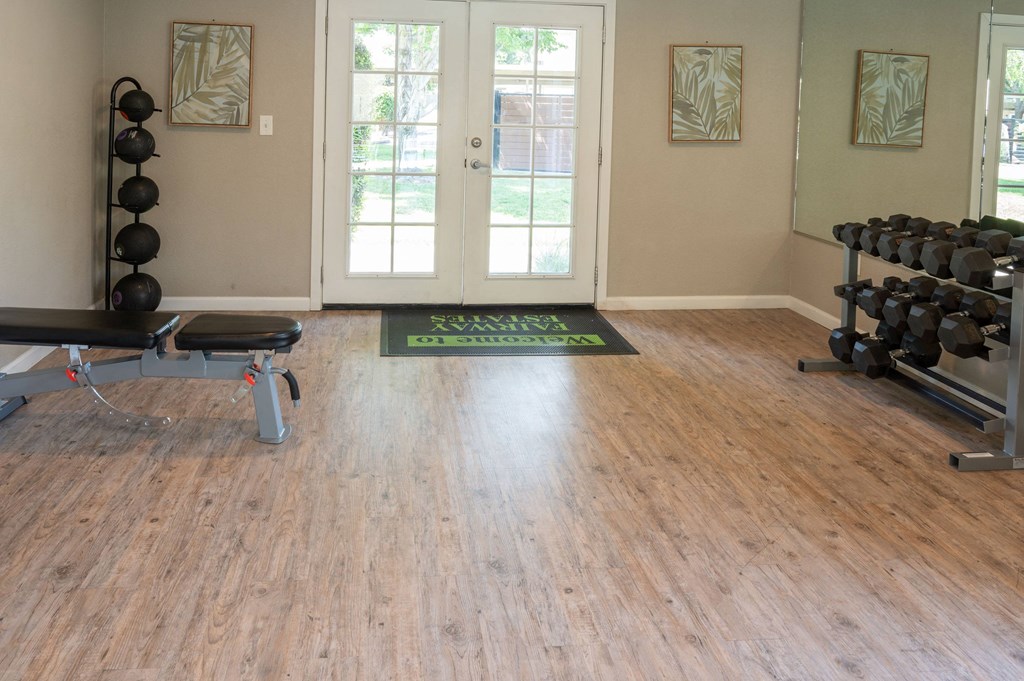 a fitness room with weights and a rug on a wood floor