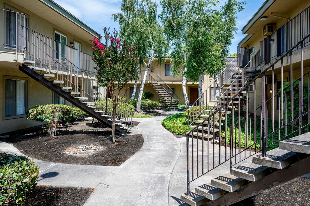a courtyard with stairs and trees in front of an apartment building