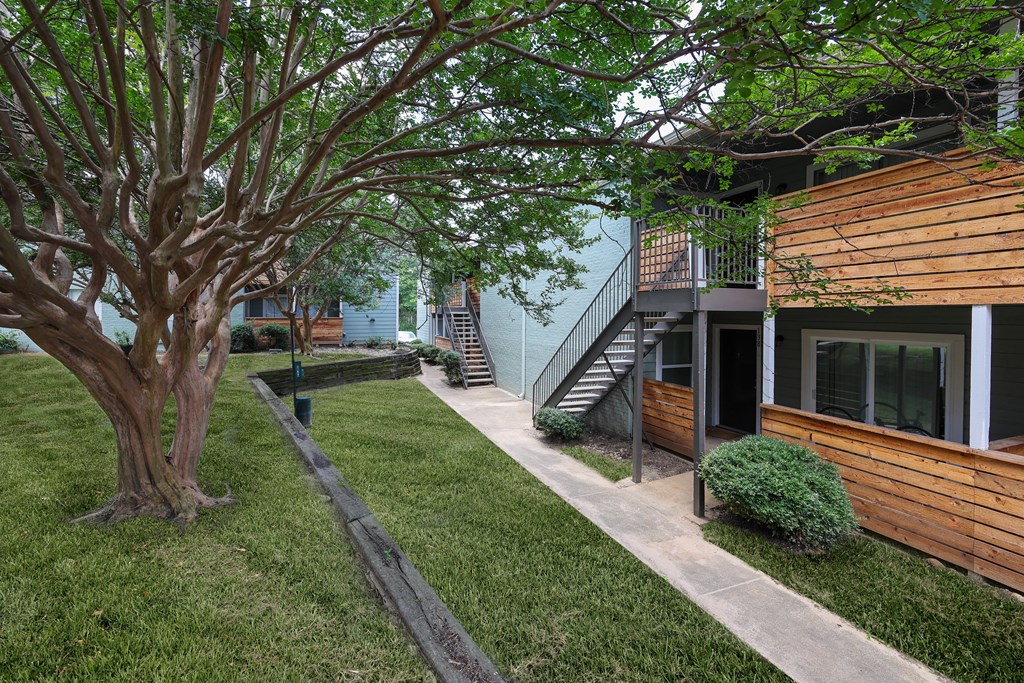 Exterior view of building with sidewalk winding through lush grass and trees