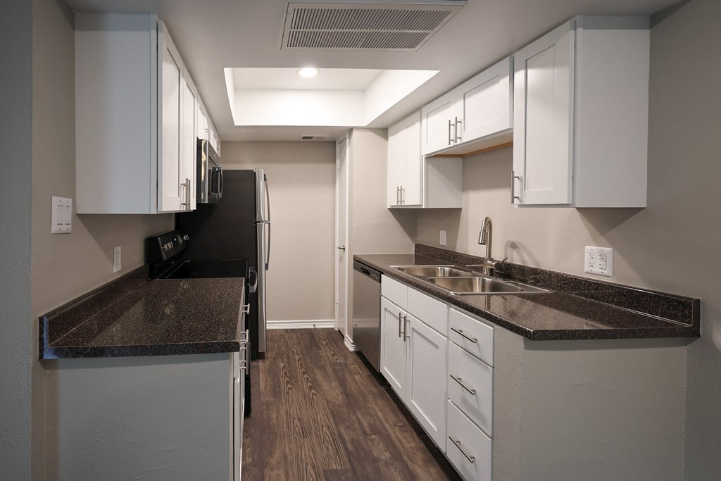 View of kitchen with whit cabinets, stainless appliances, dark counters, and wood look floorin
