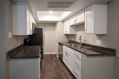 View of kitchen with whit cabinets, stainless appliances, dark counters, and wood look floorin