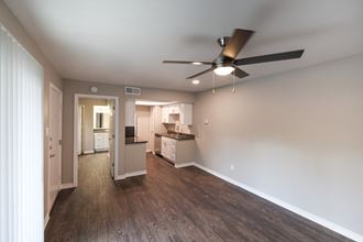 View from living area into kitchen and bedroom. Ceiling fan in living area, whit cabinets and stainless appliances in kitchen