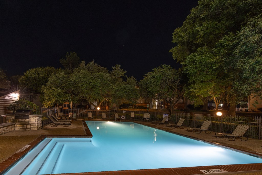 View of the pool at night with lounge chairs and seating