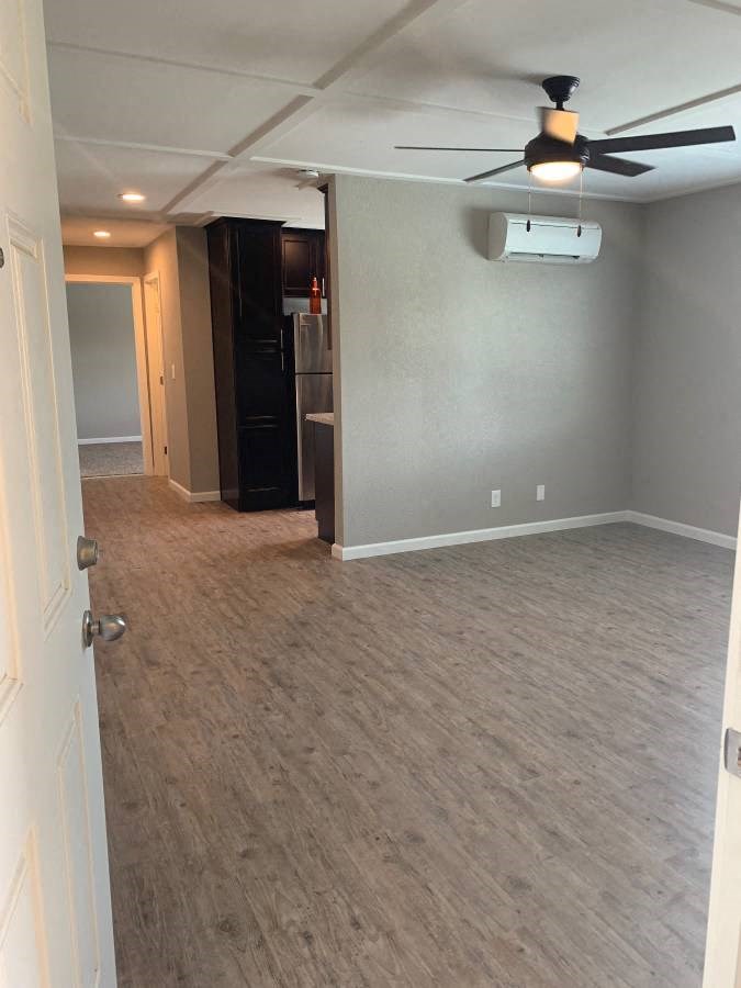 Living area view with peak into kitchen and hallway to bedroom, with wood look flooring, ceiling fan, and AC