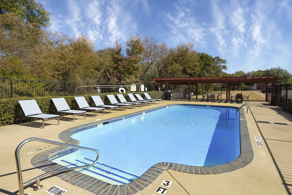 View of gated second community pool with lounge chairs, pergola covering grilling station with counters to meal prep, and seating.