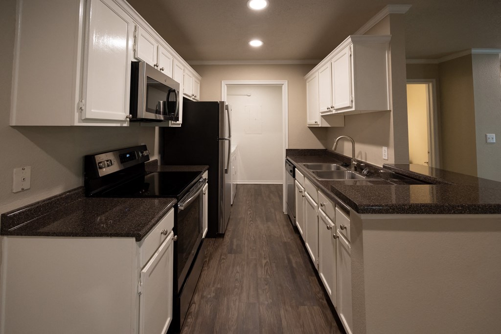 Vies of Tuscany - Chablis - Sonoma kitchen with dark counters, stainless appliances, white cabinets, wood look flooring and view into utility room with washer and dryer included