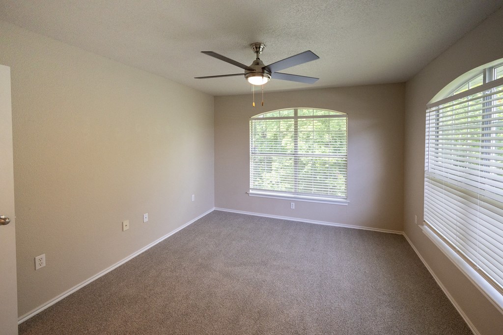 View of upstairs corner unit with two well lit windows, ceiling fan, and carpet flooring.