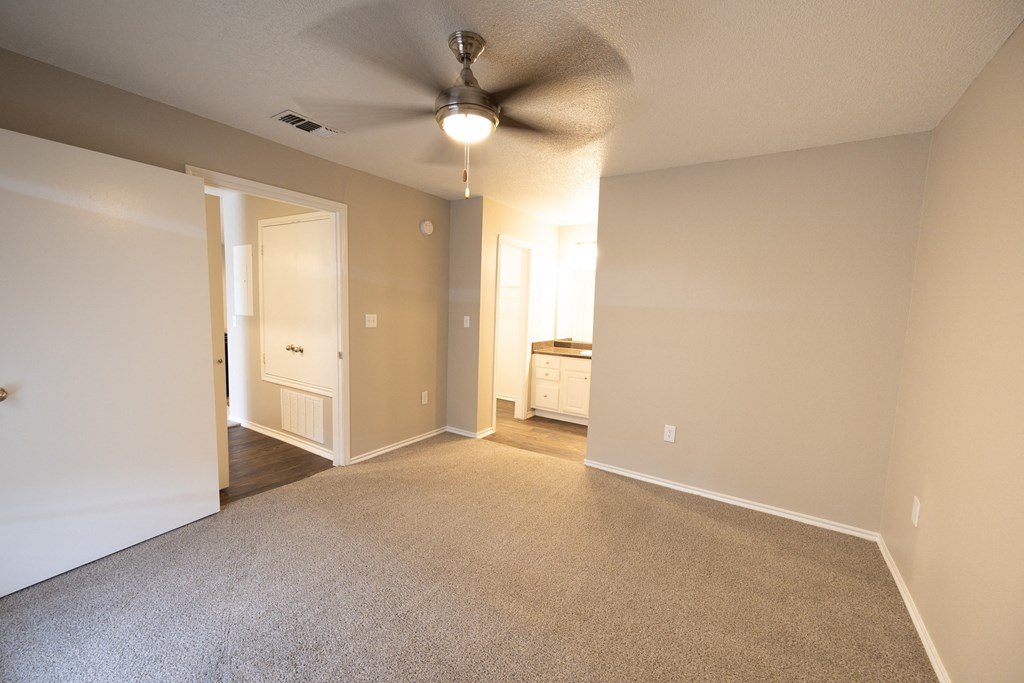View of main bedroom looking into ensuite bathroom with carpet flooring, ceiling fan, and view in to hallway