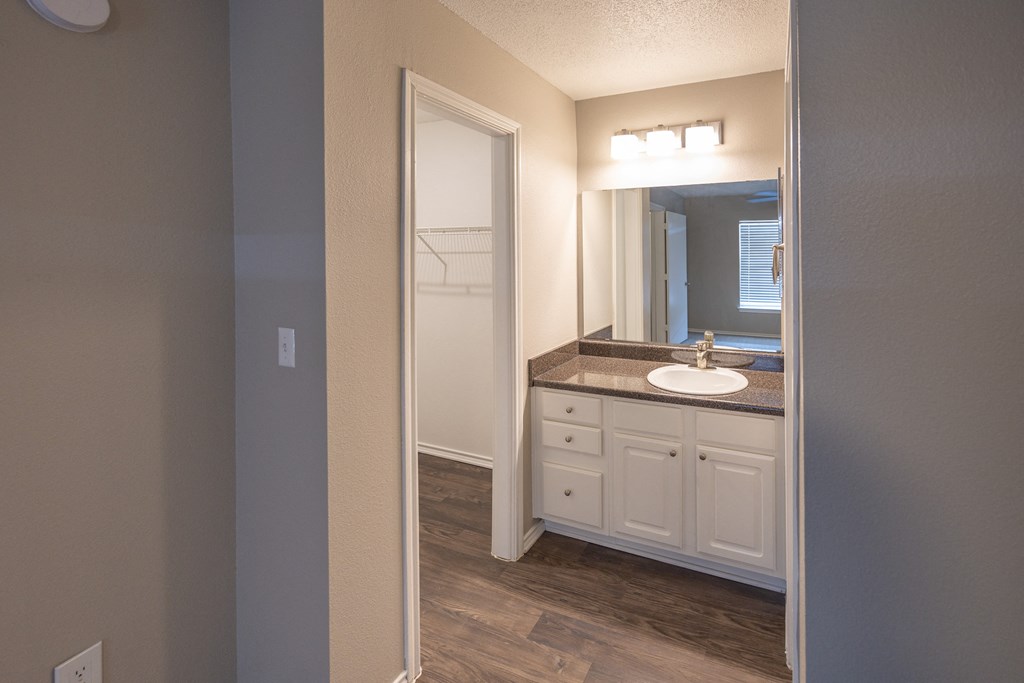 View of ensuite bathroom vanity with counter space, large mirror, and view into walk in closet