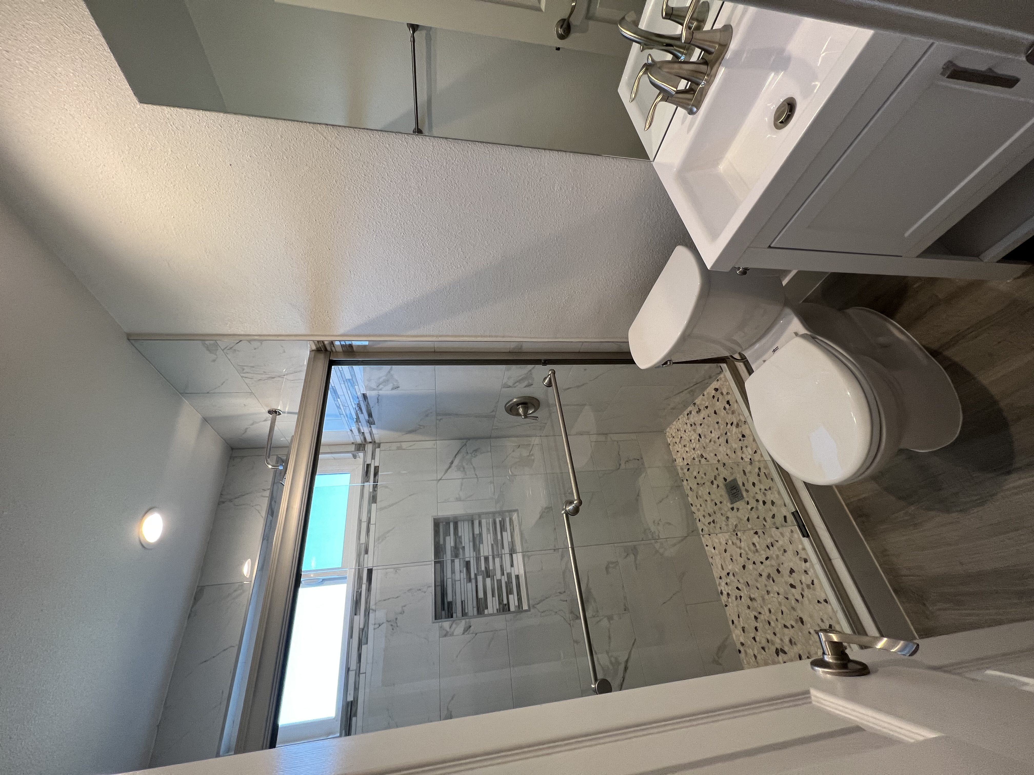 View of bathroom with walk in tile shower, well lit window above, toilet, and sink