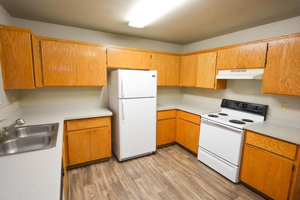 View into kitchen with wood look flooring, white appliances, light counters, and wood cabinets