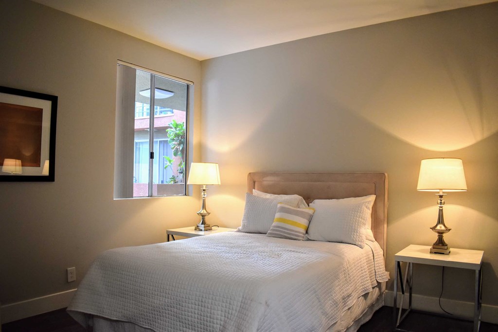 View of model bedroom with well lit window, and bedroom furniture