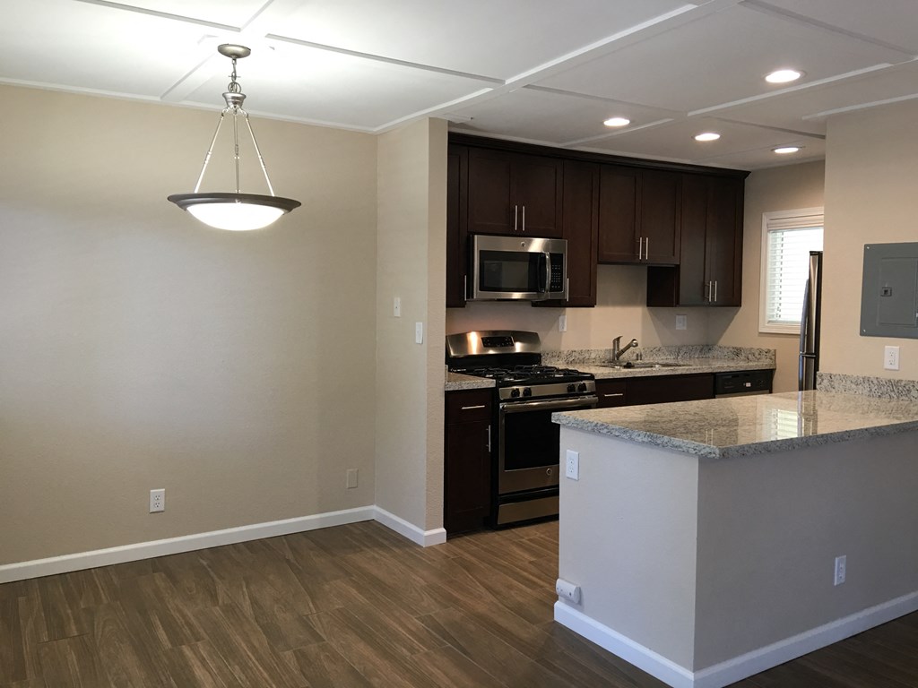 view of kitchen and dining area with wood look flooring, stone counters, stainless appliances, brown cabinets, recessed lighting, and a chandelier in the dining area