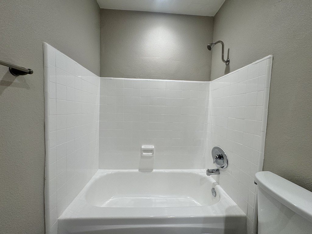 A white bathroom with a white tub and a white shower head.