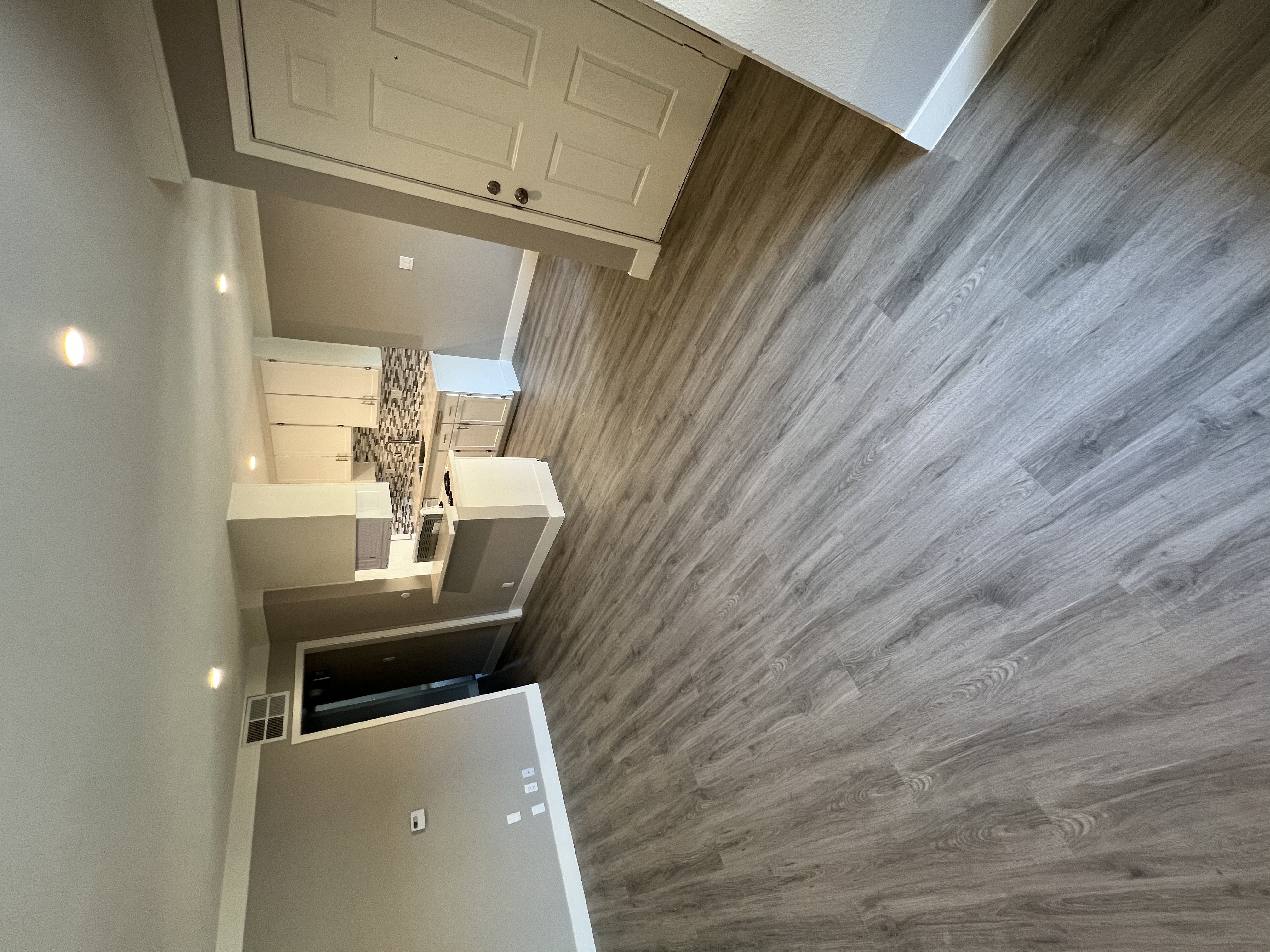 View into living area, dining area, and kitchen. Has recessed lighting, wood like flooring, and white cabinets.