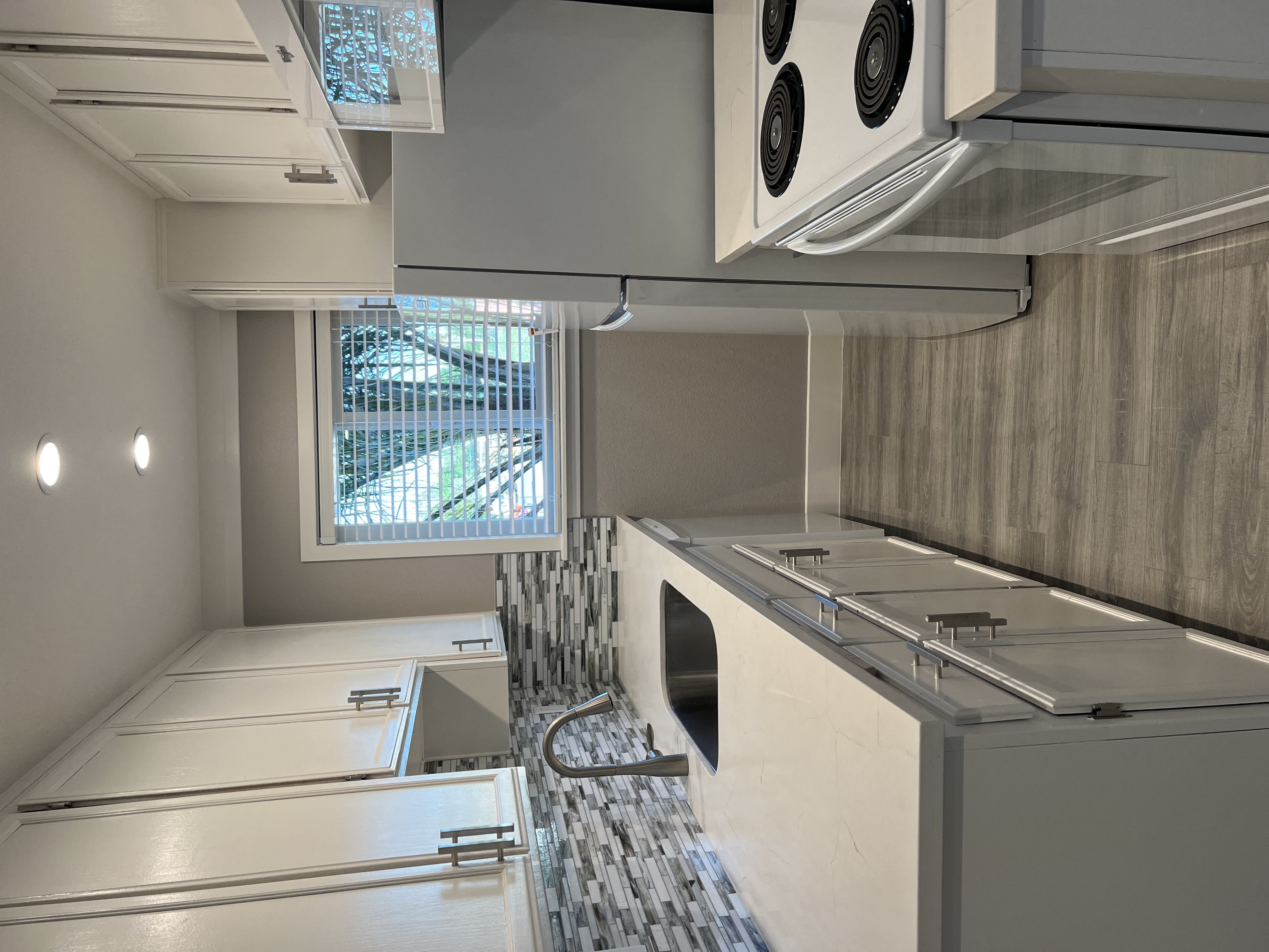 View kitchen with window at end, white cabinets, white countertops, inlaid sink, white appliances, with wood look flooring.