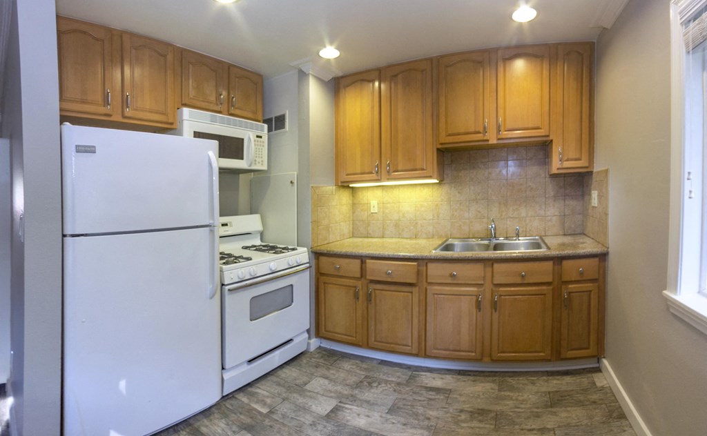 View of kitchen with wood look flooring, white appliances, brown cabinets