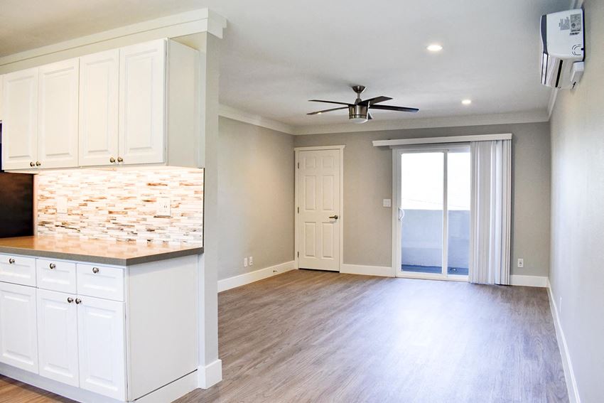 View of living area with wood-like flooring, ceiling fan, entrance to patio, and partial view of kitchen counter and cabinet at Americana La Crescenta - Photo Gallery