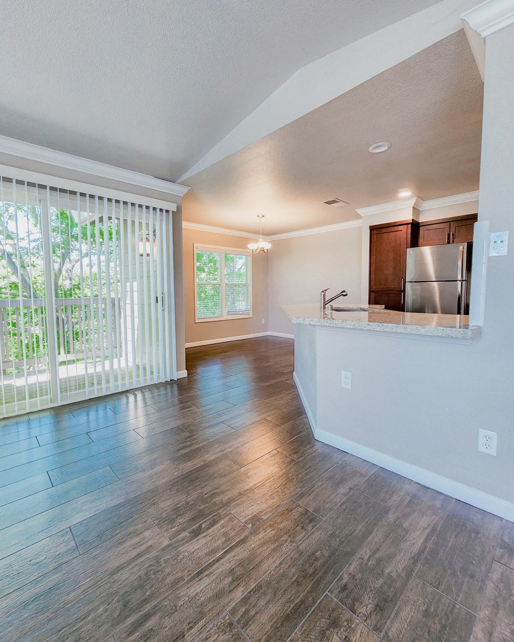 View into kitchen and dining area with access to private balcony, wood look flooring, brown cabinets, stainless appliances, and stone counters